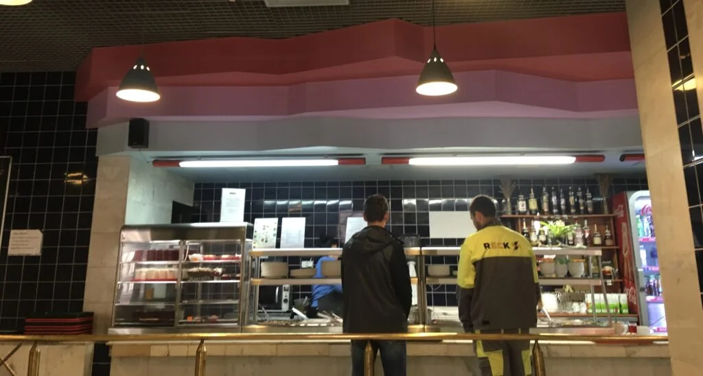 two men line up for food at a counter at a latvian canteen in riga