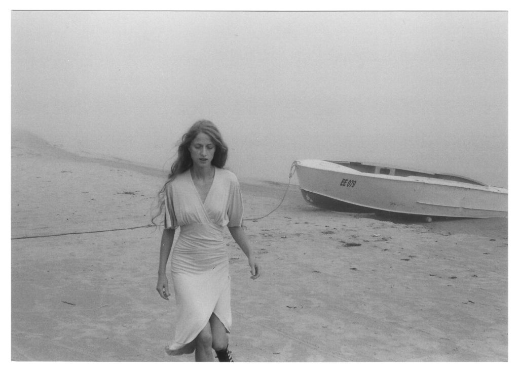 woman walks by the sea with boat in background